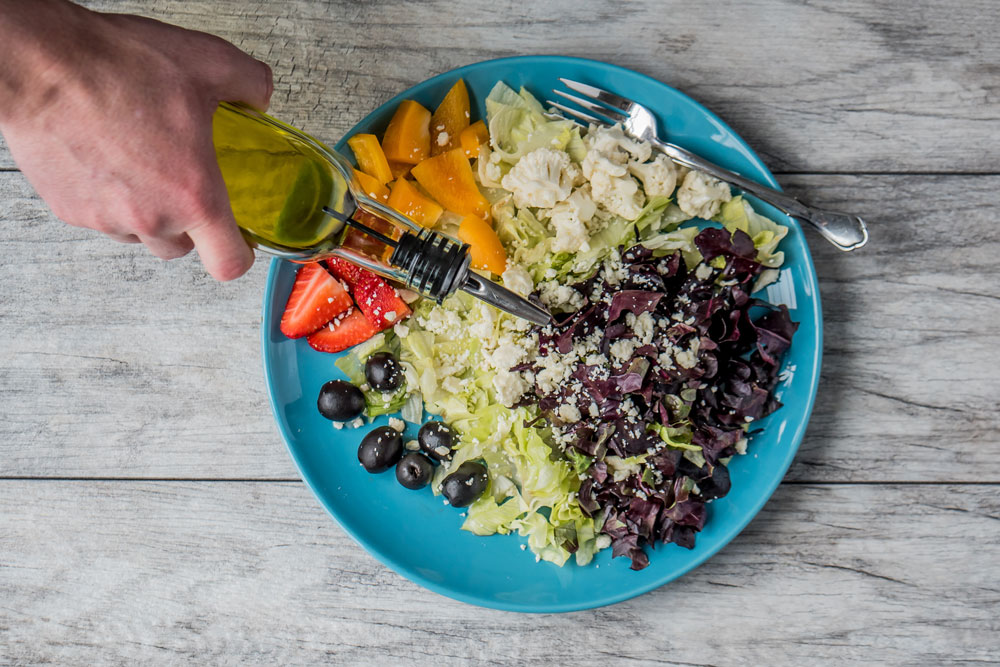 prato com mix de vegetais e mão de pessoa adicionando azeite, vista superior